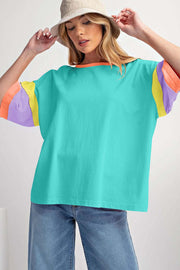 Green Color Block Oversize Top with round neckline and colorful sleeves, worn with jeans and a hat.