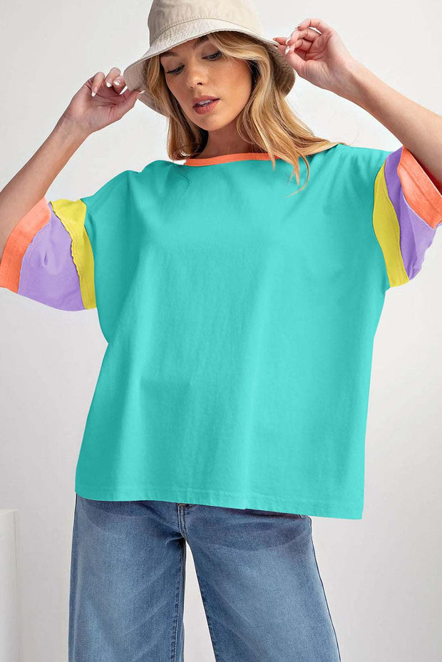 Green Color Block Oversize Top with round neckline and colorful sleeves, worn with jeans and a hat.