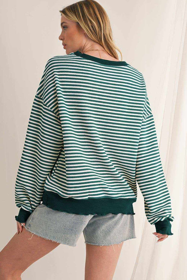 Woman wearing a green and white striped drop shoulder long sleeve top with dark green cuffs and hem paired with denim shorts.