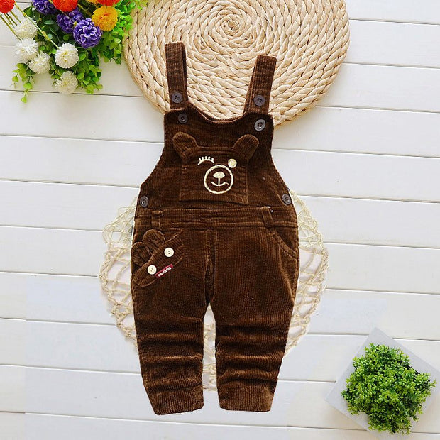 Children brown overalls with cartoon bear design, adjustable straps, and multiple pockets, on a decorative background.