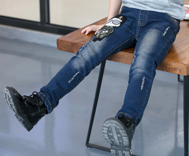 Boys wearing blue jeans sitting on a wooden bench.