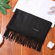 Elegant black designer scarf shawl on wooden table, showcasing intricate fringe detailing.