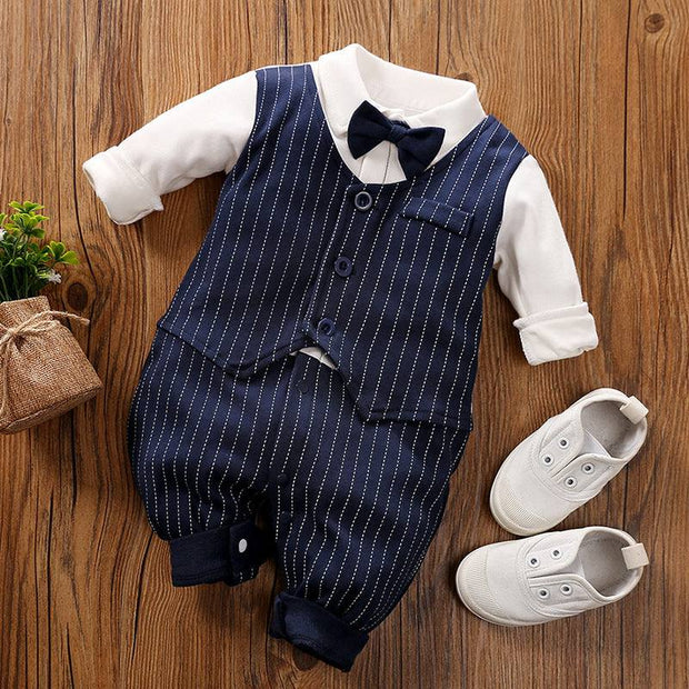 Baby Gentleman Jumpsuit with bowtie and striped vest, paired with white shoes on wooden floor.