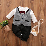 Baby Gentleman Jumpsuit with bowtie and vest detail on wooden floor.