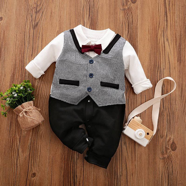 Baby Gentleman Jumpsuit with bowtie and vest detail on wooden floor.