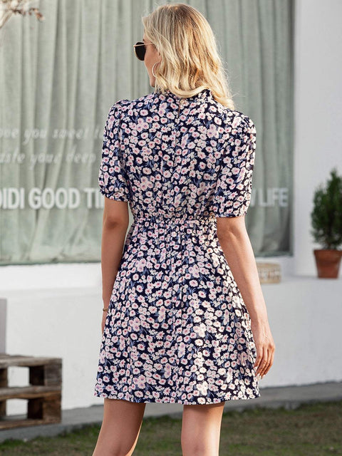 Woman wearing Ivy Lane Floral Mini Dress with pink and white flowers on navy background, standing outdoors