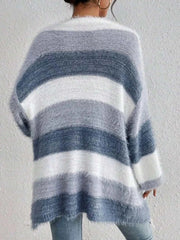 Back view of a fluffy open front striped knit cardigan in shades of gray and white worn by a person against a plain wall background
