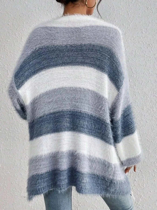 Back view of a fluffy open front striped knit cardigan in shades of gray and white worn by a person against a plain wall background