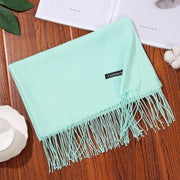 Mint green designer scarf shawl with tassels on wooden table.