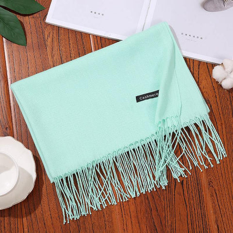 Mint green designer scarf shawl with tassels on wooden table.