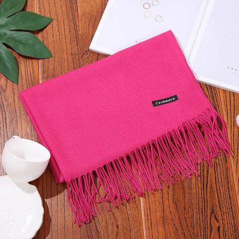 Pink designer scarf shawl with fringed edges, laid on a wooden surface.