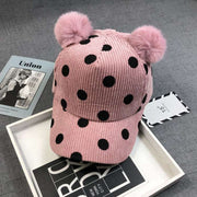 Pink ball peaked hat with black polka dots and two hairball pom-poms.