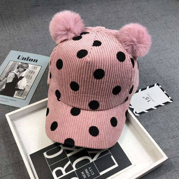 Pink ball peaked hat with black polka dots and two hairball pom-poms.