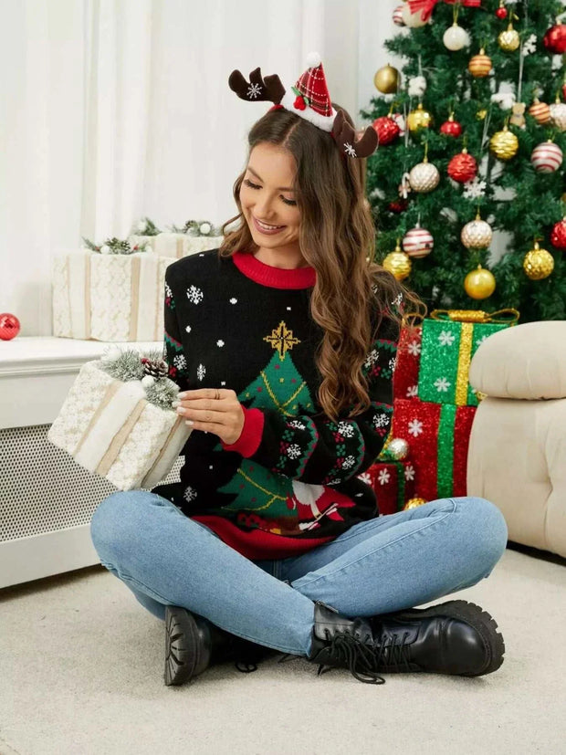 Woman wearing Christmas Tree Santa Round Neck Sweater sitting by decorated Christmas tree holding a gift box
