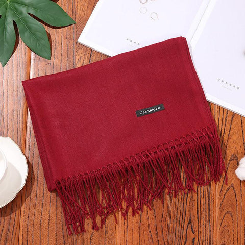 Red designer scarf shawl on wooden surface with fringe detailing.