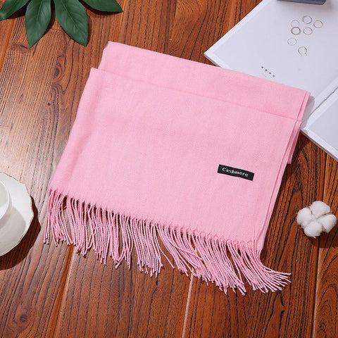 Pink designer scarf shawl with fringe detail on a wooden surface, showcasing its luxurious and versatile design.
