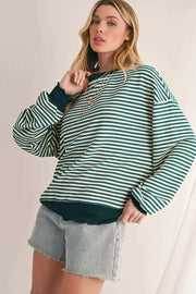 Woman wearing green and white striped drop shoulder long sleeve top with green cuffs and hem paired with denim shorts