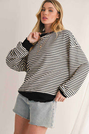 Woman wearing a black and white striped drop shoulder long sleeve top with black cuffs and hem paired with light denim shorts