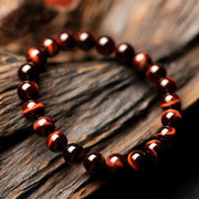 Red Tiger Eye Bracelet with polished red agate beads on wood background.