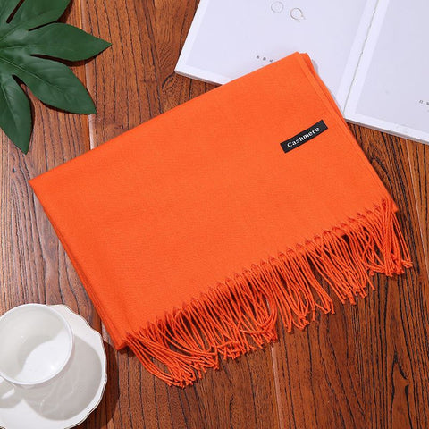 Orange designer scarf shawl on wooden table with books and teacup.