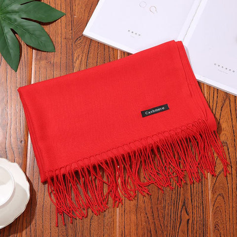 Designer scarf shawl in rich red with tassels, displayed on a wooden surface.