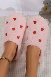 Pink heart embroidered plush slippers on feet, cozy and stylish indoor footwear.