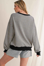 Woman wearing black and white striped drop shoulder long sleeve top with black cuffs and hem paired with denim shorts viewed from the back