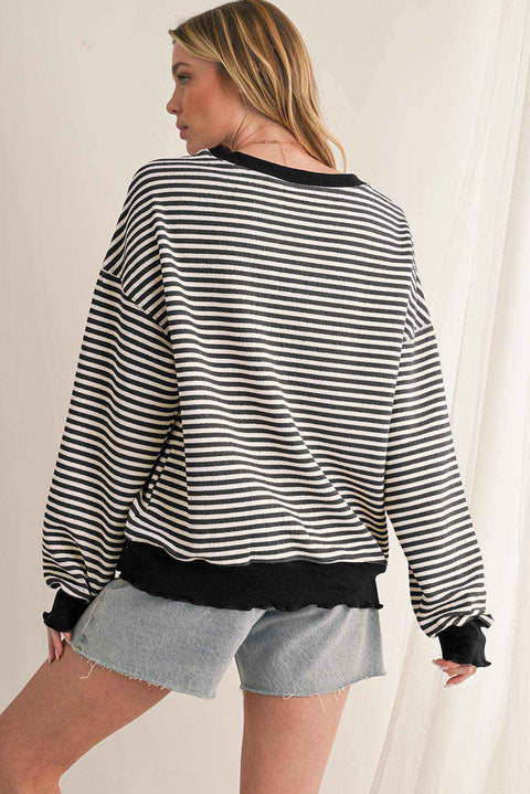 Woman wearing black and white striped drop shoulder long sleeve top with black cuffs and hem paired with denim shorts viewed from the back