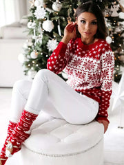 Woman wearing red and white long sleeve snowflake pattern sweater with matching socks sitting by Christmas tree