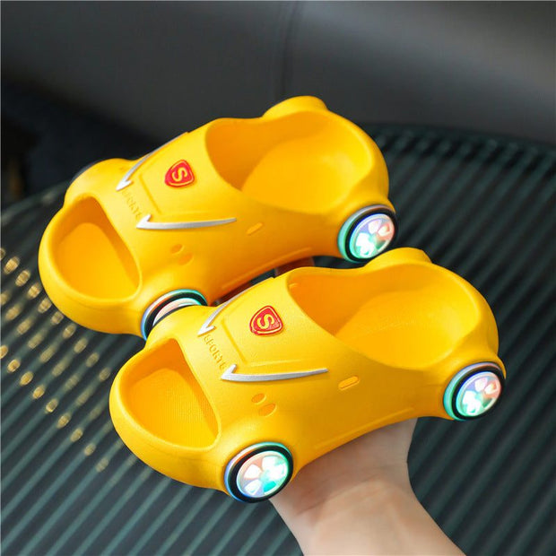 Yellow kids glowing slippers shaped like a sports car with LED lights on wheels.