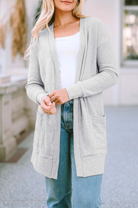 Woman wearing a pocketed open front cardigan in light gray with jeans and a white top.