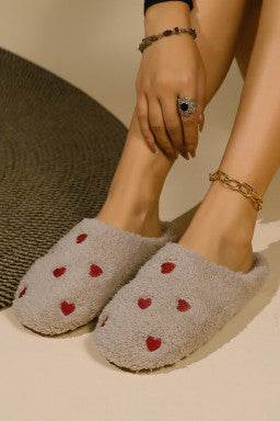 Pink heart embroidered plush slippers on feet indoors.