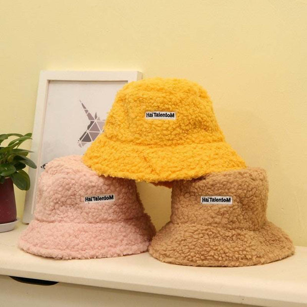 Lambswool female fishing cap trio in yellow, pink, and beige on a table.
