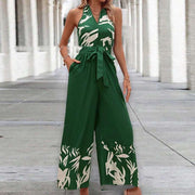 Backless halter jumpsuit in green with white floral pattern, showcasing high waist and flowing trousers.