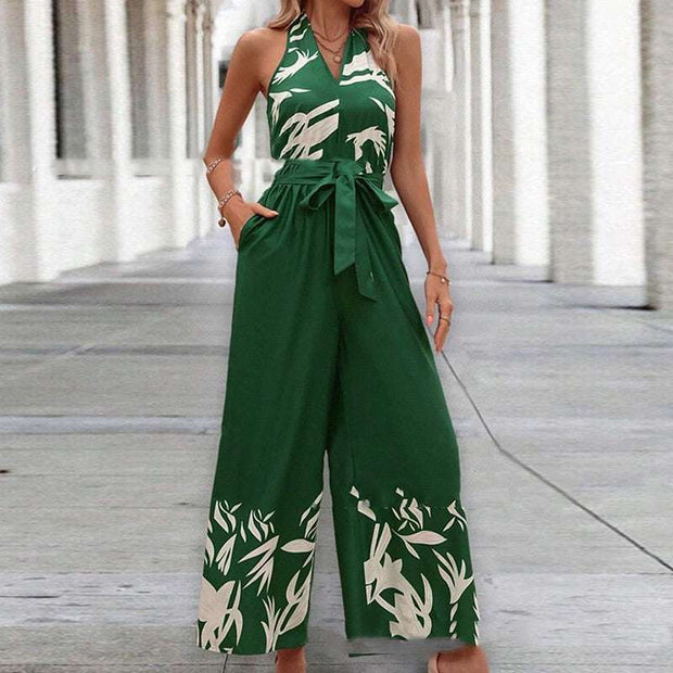 Backless halter jumpsuit in green with white floral pattern, showcasing high waist and flowing trousers.