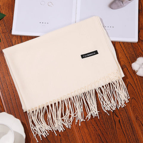 Designer scarf shawl in soft cashmere with fringe detailing, displayed on wooden table.