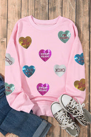 Pink graphic Valentines sweatshirt with sequin heart graphics and romantic lettering on a wooden background.
