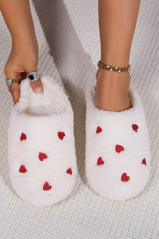 Pink heart embroidered plush slippers on a soft fabric background, featuring cozy slip-on design.