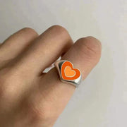 Heart-shaped ring with orange and white design on a finger; Creative Love Heart Ring.