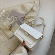 Square Chain Shoulder Bag with elegant chain strap in white, resting on a textured beige fabric, showcasing its sleek square design.