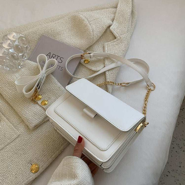 Square Chain Shoulder Bag with elegant chain strap in white, resting on a textured beige fabric, showcasing its sleek square design.