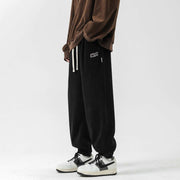 Black straight-leg sweatpants with elastic waistband and drawstring, styled with sneakers for a casual look.