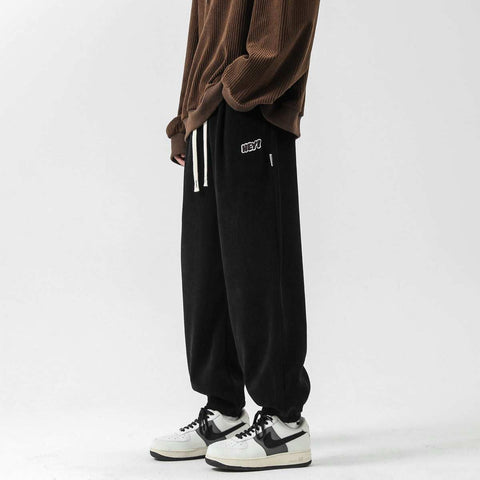 Black straight-leg sweatpants with elastic waistband and drawstring, styled with sneakers for a casual look.