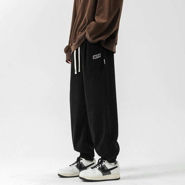 Black straight-leg sweatpants with elastic waistband and drawstring, styled with sneakers for a casual look.