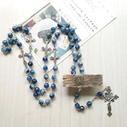 Rosary necklace with blue beads and cross pendant on light background.