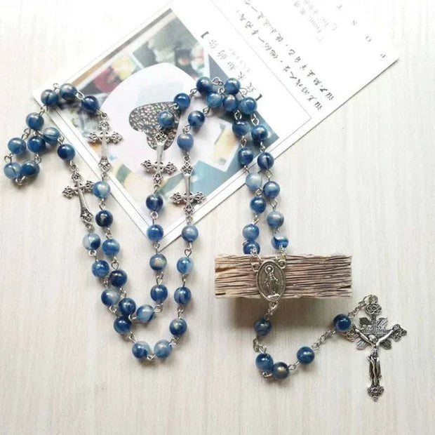 Rosary necklace with blue beads and cross pendant on light background.