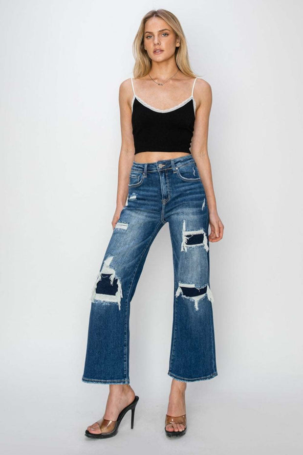 Fashion-forward individual wearing Risen Wide Leg Crop Jeans with distressed patches, showcasing high-rise fit and relaxed wide-leg design.