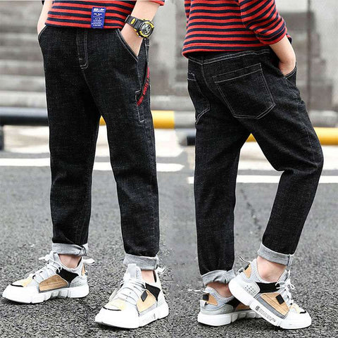 Boys wearing black denim jeans with rolled cuffs and casual sneakers, featuring a striped shirt for a trendy look.
