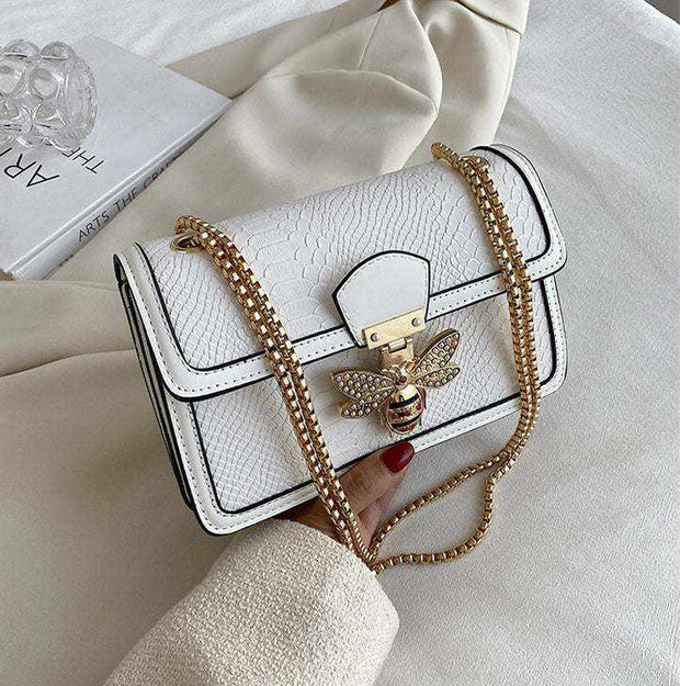 Chain Shoulder Bag with gold chain strap and stylish clasp on white fabric background.