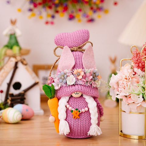 Easter Knit Faceless Doll with pink hat and floral accents displayed on a wooden table among Easter decorations.